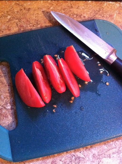dehydrating tomatoes tomato cut into quarters sitting next to a knife on a chopping block