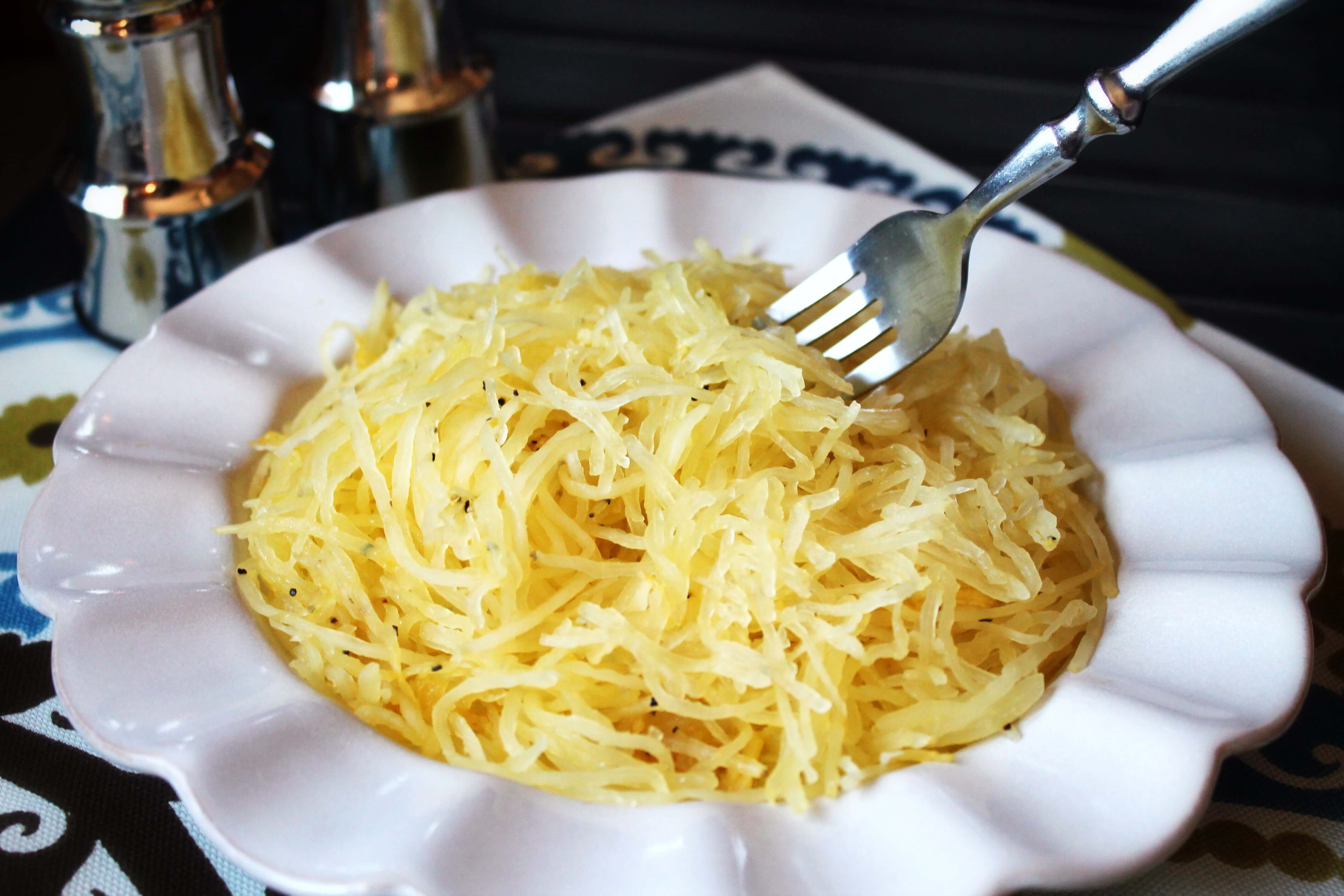 How to Cook Spaghetti Squash 7 white bowl filled with cooked spaghetti squash. A fork is poised above the bowl ready to eat.