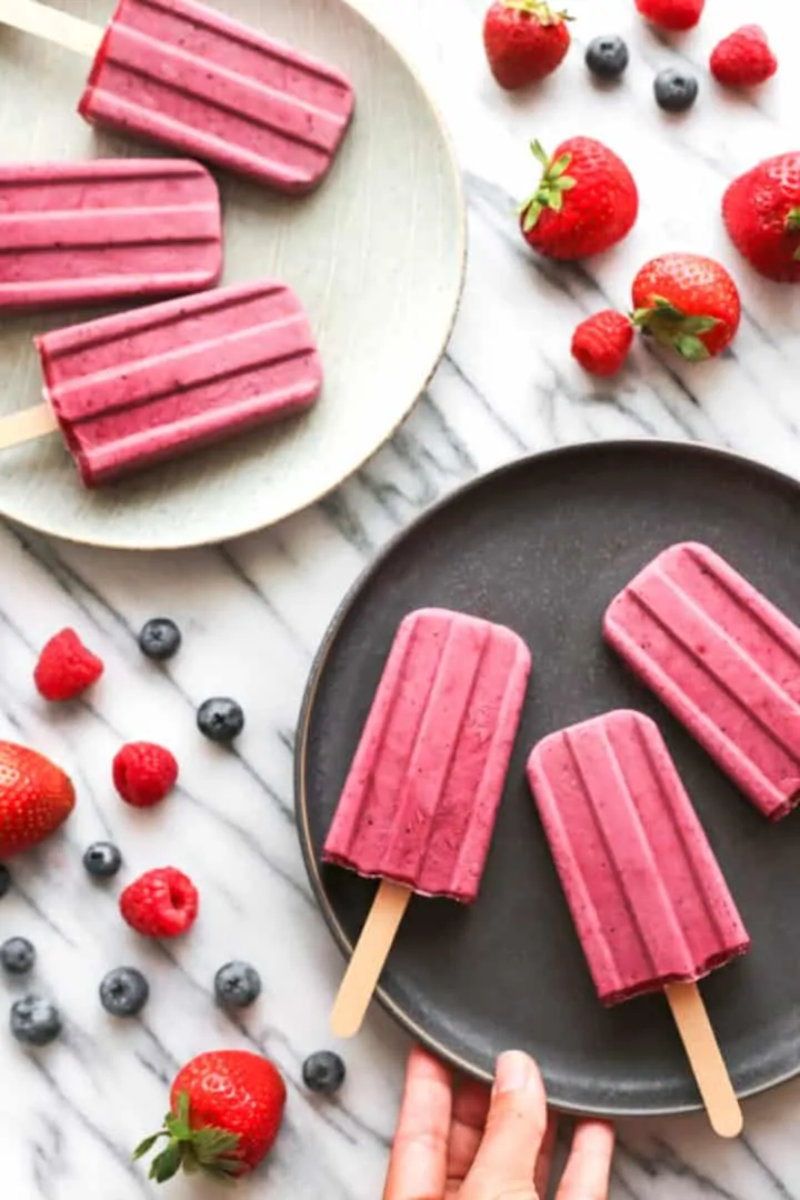 Don't Miss These Recipes Using Coconut Yogurt 3 Mixed Berry Coconut Yogurt Popsicles from Dish by Dish arranged on a dark plate and a light plate. Surrounded by loose berries.