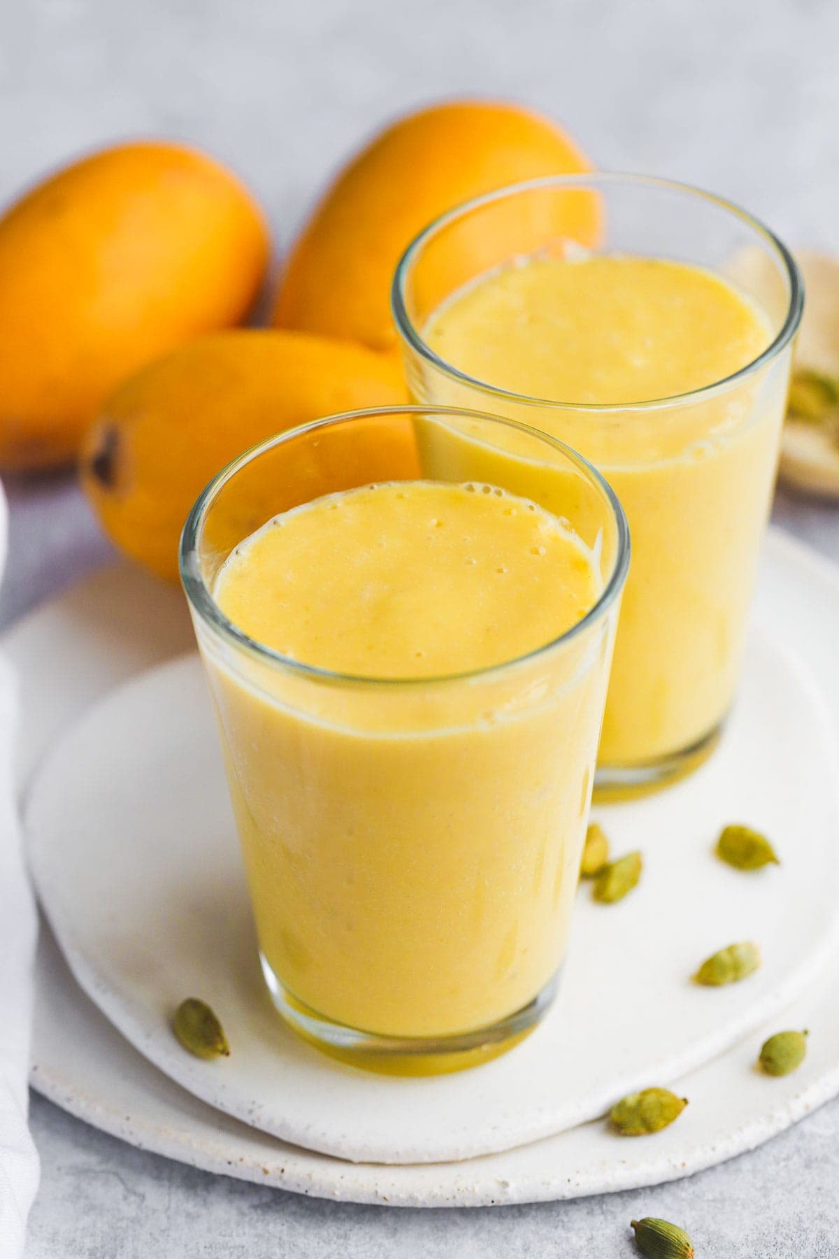 Don't Miss These Recipes Using Coconut Yogurt 5 2 glasses of vegan coconut yogurt mango lassi sit on a plate surrounded by cardamom pods and mango.
